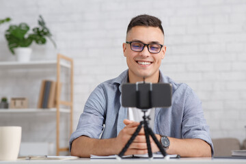 Modern work from home remotely during covid-19 outbreak. Smiling man with glasses looks at smartphone on tripod and makes recording or video call