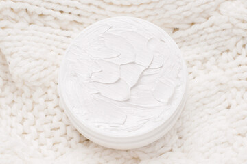 Winter face and body care concept. Organic cream on a knitted white sweater. View from above