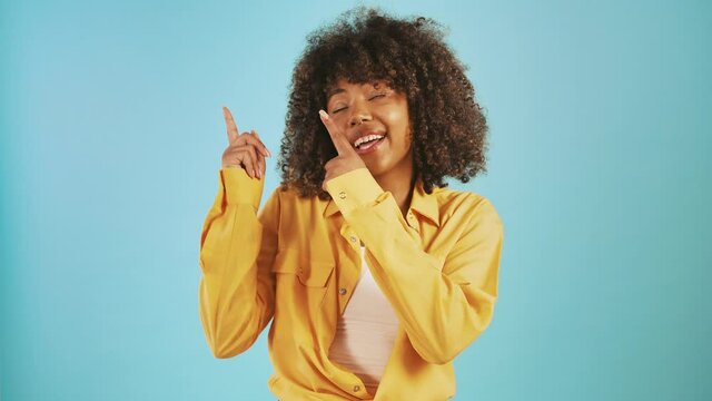 African-american young female pointing up by her forefingers asking you to look, smiling posing on blue background