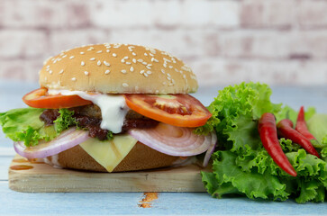 
Pork burger with cheese, onion, tomato and lettuce on a wooden cutting board