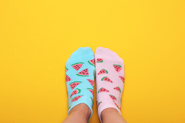 Female feet in pink and blue socks in watermelon print on a pastel yellow background. Top view.Copy...