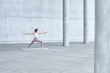Fototapeta na wymiar Frau/Mädchen in Pastell gekleidet macht Outdoor Yoga Übungen/Sonnegruß in moderner Beton Architektur. Urbanes Leben. 