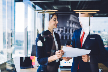 Successful male and female proud ceo discussing business strategy for financial project analyzing paper report in office workspace, formally dressed colleagues talking about exchange productivity