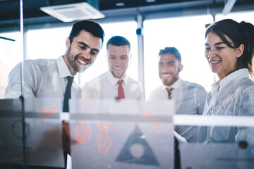 Multicultural group of corporate workers analyzing monetary gain of capital standing near glass stand with paper reports and searching negotiations for exchange experience, successful brainstorming