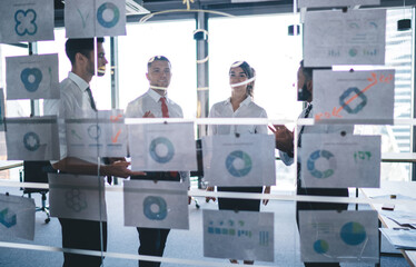 Diversity analysts in formal clothing creating marketing plan for corporate productivity, successful male and female experts brainstorming during working process with revenue infographics in office