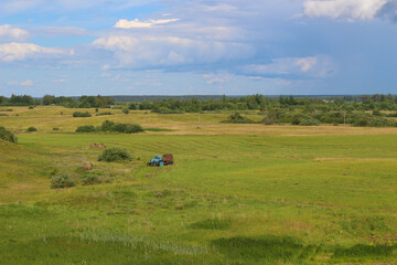 Fields with yellow-green grass against a bright blue sky with clouds. Hills in the distance.