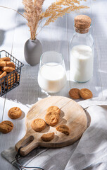 fresh homemade oatmeal cookies on wood cutting board with a glass of  milk on a white wooden table