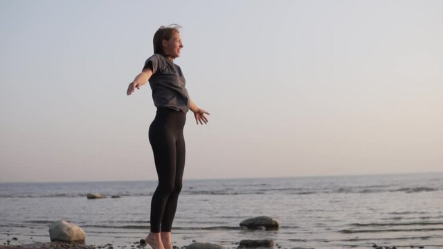 Happy Woman doing jumping jacks at sea, practice sports outdoors in times of pandemic.