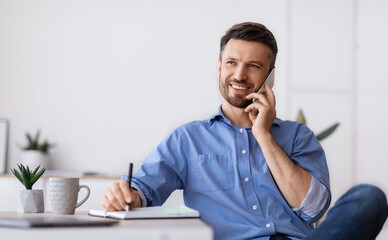 Business Communication. Successful Businessman Sitting At Workplace Talking On Cellphone With Client