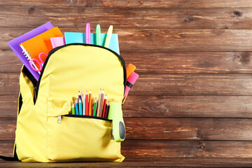 Backpack with school supplies on brown wooden background