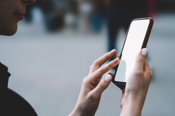 Crop anonymous young woman reading message on smartphone in street