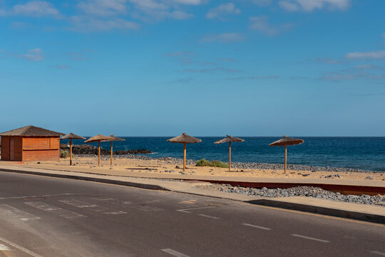 Road with old pedestrian crossing towards a golden manmade sand beach near the Atlantic with straw umbrellas or palapas and a chiringuito, deserted coast in San Blas, Tenerife, Canary Islands, Spain