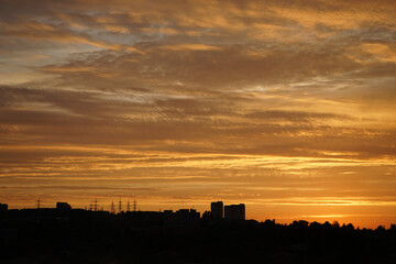 Golden sunset over the city. Silhouettes of buildings and trees on the horizon against the background of the sky with clouds. Colorful orange yellow red sunset background.