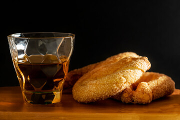 Close up of sweet donuts with sugar and a glass of rum on wooden board and black background