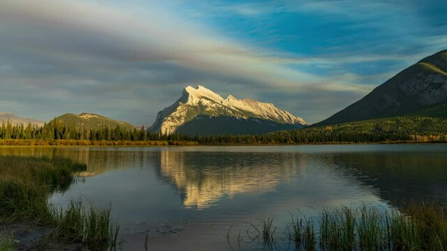 Mount Rundle, Sulphur Mountain in sunset time. View from Vermilion Lakes lakeshore. Yellow leaf forest on lake shore in autumn season sunny day. Banff National Park, Alberta, Canada. Time-lapse 4K UHD