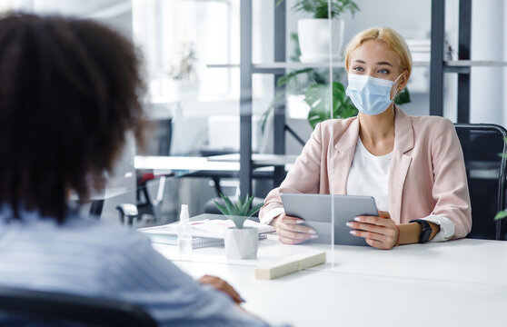New normal and modern interview during covid-19 outbreak. HR manager with laptop looks at african american woman through protective glass - Powered by Adobe
