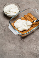 tiramisu dessert cooking - Traditional Italian Savoiardi ladyfingers Biscuits and cream in glass baking dish on concrete background