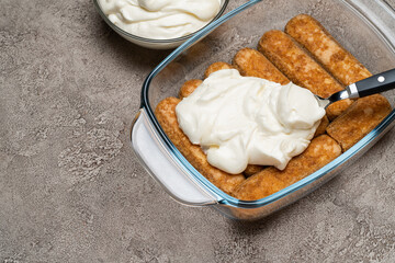 tiramisu dessert cooking - Traditional Italian Savoiardi ladyfingers Biscuits and cream in glass baking dish on concrete background
