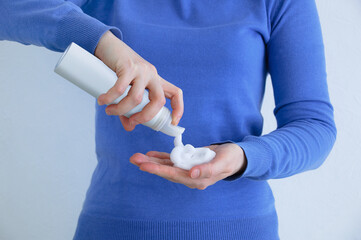 Caucasian woman blue sweatshirt squeezes styling foam into her hand.