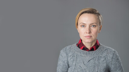 Fototapeta premium young woman with short hair, natural makeup over light grey background. Indoor portrait of beautiful blonde young woman in knitted sweater