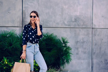 Smiling woman with shopping bags talking on smartphone on street