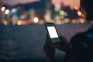 Crop young woman using smartphone with copy space screen on background of blurred cityscape at night