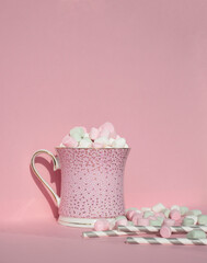  Mug with hot cocoa and marshmallows on top. Festive hot drink Pink background. Pink mug. Paper cute straws for drinks and tender marshmallow cubes. Copy space for text.