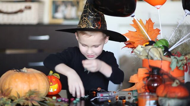 funny kid boy in witch hat for Halloween party have fun at home. Child playing with Halloween toys.