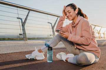 Smiling female runner is texting a message while having a break after training.