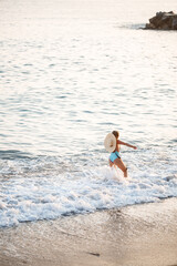 Beautiful girl in a blue swimsuit and hat on a sandy beach at the sea in the sunset sunlight