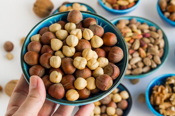 Hand holding a blue ceramic bowl full of nuts aganist other bowls,close up taken