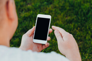close-up shot of male hands holding smartphone with blank screen copy space for your text message or information content, against green nature background