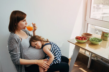 child girl sitting on the legs of a pregnant mother and communicating with the child in the woman's...