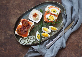 Open sandwiches with dark rye bread with cheese, salmon fish and dried tomatoes.Healthy natural breakfast on a wooden ancient brown background.Side view.