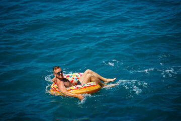 A young man swims in the open sea on an inflatable ring on a sunny day. Summer vacation, tourist on vacation