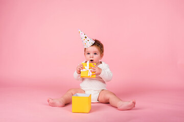 a little girl with a holiday hat sits with a yellow box on a pink background with space for text