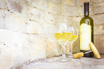 Set up of gerogian white wine Mildiani with cork and two full glasses in bright brick wall background. Blank space wine vintage production background.