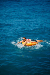 a man lies on a large inflatable rubber circle and floats on the blue sea on a bright sunny summer day