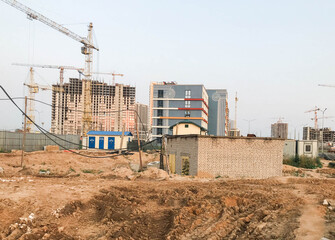 abandoned construction site. in the distance, construction cranes are building houses. there is a lot of sand on the site, abandoned houses without windows and doors