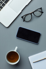 Above view flat lay of laptop and smartphone on grey workplace background with coffee cup, copy space