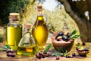 Ripe natural olives with bottles of olive oil on a vintage old wooden table on a background of olives garden.