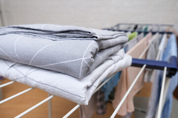 Fresh washed bed linen stacked, piled on a dryer, dry apparel on a folding portable dryer close up, housekeeping, homework and chores concept