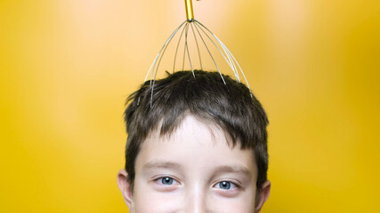 A caucasian boy enjoy head scalp massage by anti stress acupuncture metal octopus tool, equipment, she closes her eyes with pleasure, yellow background, close up view