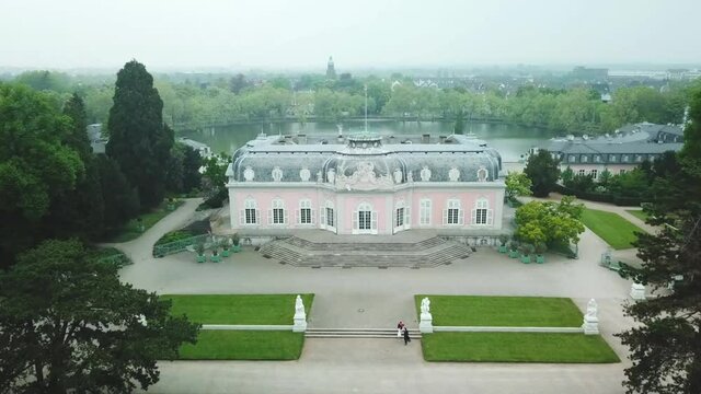 Smooth fly over Benrath Palace with the lake and park behind surrounded by trees on a foggy day.
