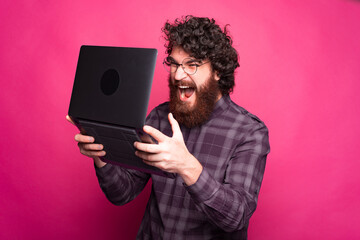 Photo of angry bearded man looking at laptop and screaming