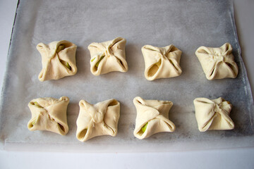 Puff cookies or corners with apples lie on parchment paper. Products from raw dough are ready for baking. View from above