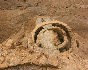 the middle terrace of the northern palace on a cloudy day at masada in israel from above with part of the lower terrace visible and a roman camp in the background