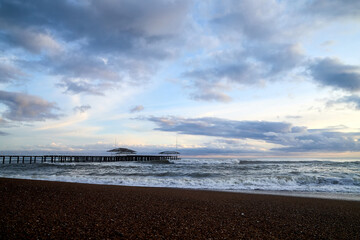 View from beach to water of sea, waves with white foam, pierce and sky with clouds in a nice evening.