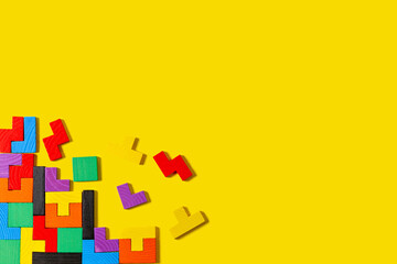 Different colorful shapes wooden puzzle blocks on yellow background. Geometric shapes in different colors, top view