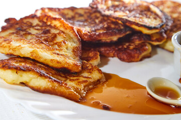 Pancakes on white plate and sweet liquid honey or caramel with a small spoon and with background. Delicious fried flour food. Unhealthy and harmful, but very tasty food.